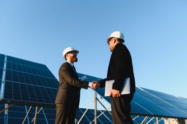 Güneş enerjisi santralinde el sıkışan iki mühendis yenilenebilir enerji geliştirme anlaşmasını imzalıyor.