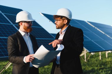 Planları inceleyen ve bir güneş enerjisi santralinde proje detaylarını tartışan iki mühendis, yenilikçi yenilenebilir enerji çözümleri üzerinde işbirliği yapıyorlar.