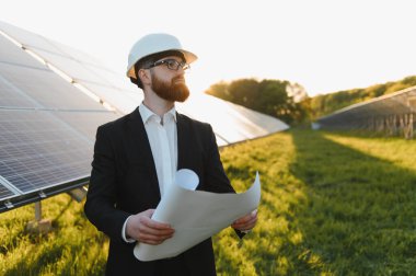 Güneş paneli çiftliğinin planlarını canlı günbatımında değerlendiren takım elbiseli bir yatırımcı.