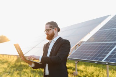 Günbatımında güneş paneli tarım yatırımlarını analiz eden bir iş adamı, sürdürülebilir enerji ve finansal büyümeyi temsil ediyor