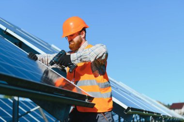 Erkek mühendis güneş enerjisi çiftliğinde tornavida kullanarak fotovoltaik paneller kuruyor ve yenilenebilir enerji üretimi için çalışıyor.