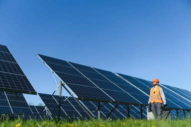 Elektrik santralindeki fotovoltaik güneş panellerinin yanında yürüyen bir mühendis, sürdürülebilir enerji üretiminin etkinliğini ve işleyişini kontrol ediyor