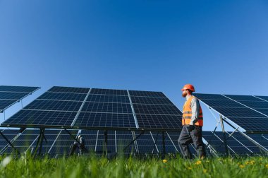 Açık bir günde fotovoltaik güneş panelleri yakınında yürüyen mühendis, alternatif enerji kaynağının işleyişini denetliyor ve kontrol ediyor