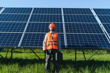 Yeşil bir alanda güneş panelleri önünde duran ve yenilenebilir enerji ve sürdürülebilirliği temsil eden alet çantalı erkek mühendis