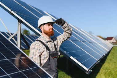 Sakallı mühendis, güneş panellerini sürdürülebilir enerjinin büyümesini temsil eden bir güneş enerjisi istasyonuna yerleştirirken kaskını düzeltiyor.