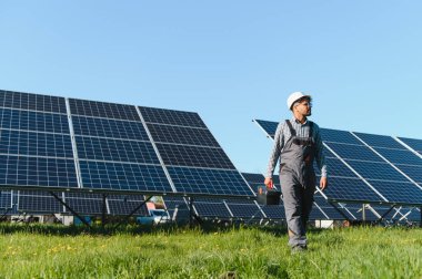 Güneşli bir günde yeşil bir alanda fotovoltaik güneş panellerinin yanında yürüyen orta doğu mühendisi.