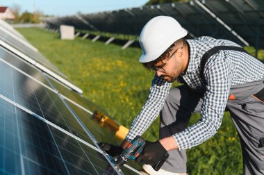 Yeşil alana güneş panelleri kuran, sürdürülebilir enerji ve çevresel korumayı temsil eden tornavida kullanan mühendis