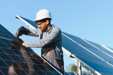 Açık mavi gökyüzü altında güneş panelleri kurmak için araçlar kullanan teknisyen, sürdürülebilir enerji çözümleri ve profesyonel zanaatkarlık sergiliyor