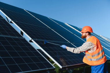 Erkek teknisyen güneş panellerini güneş enerjisi istasyonunda cam sileceğiyle temizliyor ve maksimum enerji verimliliğini sağlıyor.