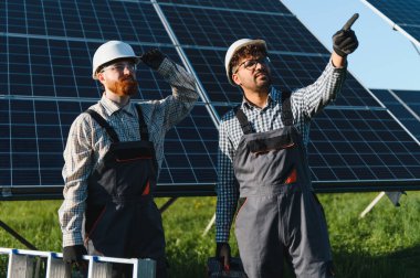 Miğferleri ve araçları olan iki mühendis yeşil bir alana güneş panelleri kurmayı tartışıyorlar.