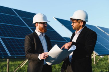 Bir güneş enerjisi santralinin planlarını inceleyen iki mühendis yenilenebilir enerji gelişimi ve sürdürülebilir enerji çözümlerini tartışıyorlar.