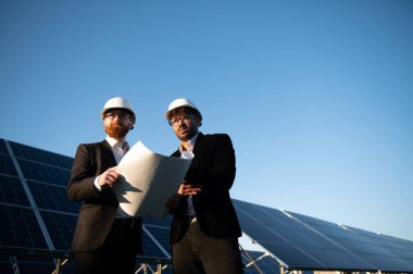 Bir güneş enerjisi santralinin planlarını inceleyen iki mühendis, yenilenebilir enerji gelişimi ve sürdürülebilir uygulamaları sembolize ediyor