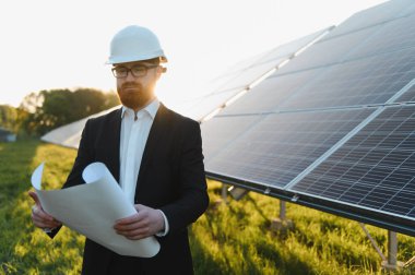 Fotovoltaik elektrik santrali yatırımlarını gün batımında değerlendirirken elinde taslak taslak olan mühendis.