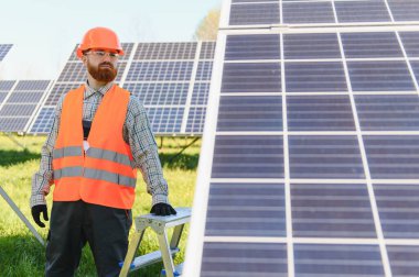 Erkek mühendis güneş panellerini bir güneş çiftliğine kuruyor, sürdürülebilir enerji üretimine katkıda bulunuyor ve yeşil enerji çözümlerini destekliyor