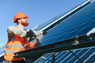Güneş enerjisi santralinde çalışan erkek mühendis güneşli bir günde tornavida kullanarak fotovoltaik paneller kuruyor.