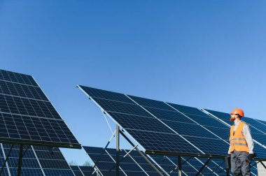 Sert şapka ve yelek giyen işçiler, açık mavi gökyüzü altında yenilenebilir enerji çözümlerine katkıda bulunarak güneş panelleri kuruyorlar