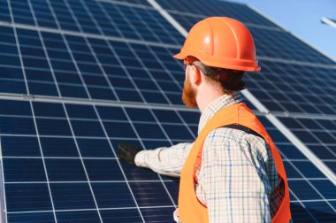 Güneş panelleri kuran, yenilenebilir enerji çözümlerini destekleyen ve açık mavi gökyüzü altında sürdürülebilir uygulamaları destekleyen güvenlik donanımlı erkek işçiler