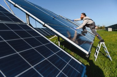 Erkek teknisyen güneş panellerini uzun bir fırçayla temizliyor ve büyük bir güneş çiftliğinde maksimum enerji verimini sağlıyor.