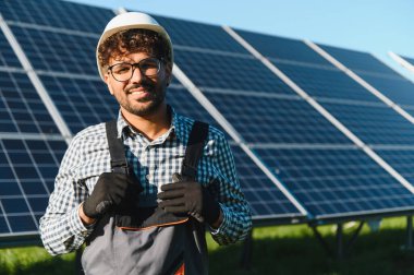 Yenilenebilir enerji santralinde fotovoltaik panellerle çalışırken gülümseyen mühendis, sürdürülebilirliği ve temiz enerji çözümlerini destekliyor