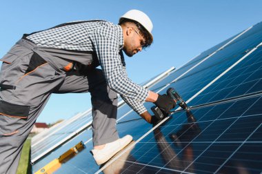 Koruyucu ekipman teknisyeni çatıya güneş panelleri kurmak için araçlar kullanıyor, yenilenebilir enerji çözümleri ve sürdürülebilir teknoloji gösteriyor