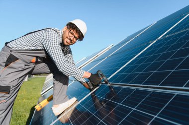 Güneşli bir günde güneş paneli kuran güvenlik kasklı gülümseyen mühendis yenilenebilir enerji ve sürdürülebilirliği temsil ediyor.