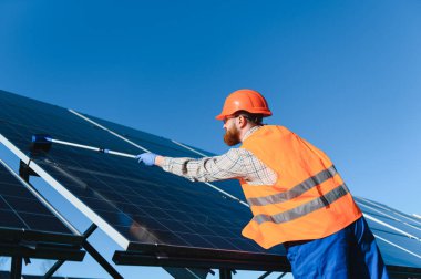 Güvenlik yeleği ve kasklı teknisyen güneş panellerini özel bir fırçayla temizliyor, maksimum enerji verimliliğini sağlıyor ve sürdürülebilir uygulamaları destekliyor