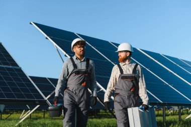 İki mühendis bir güneş enerjisi santralinde yürüyen ve araç ve ekipman taşıyor, bakım yapıyor ve yenilenebilir enerji gösteriyor