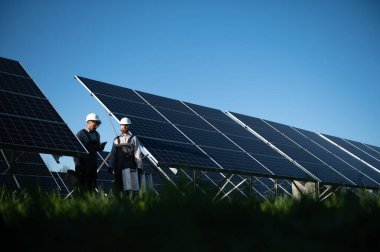 Güneş enerjisi ve sürdürülebilirliğe katkıda bulunan iki mühendis bir güneş enerjisi istasyonuna güneş panelleri kuruyor.