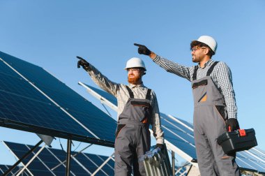 Güneş enerjisi istasyonuna güneş panelleri yerleştirirken gökyüzünü gösteren iki mühendis, sürdürülebilir bir gelecek için birlikte çalışıyorlar.