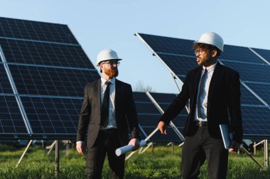 Takım elbise giyen ve güneş panelleri yakınında tartışan iki işadamı, yenilenebilir enerji ve sürdürülebilir iş uygulamaları sergiliyor