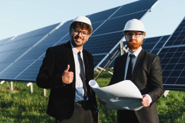 Bir güneş enerjisi santralinin planlarını inceleyen iki mühendis, başarılı yenilenebilir enerji gelişimini sembolize ediyor.