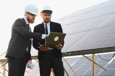 Kask takan iki mühendis, sürdürülebilir ve yenilenebilir enerji çözümleri için çalışan bir güneş paneli çiftliğini analiz etmek için dizüstü bilgisayar ve planlar kullanıyorlar.