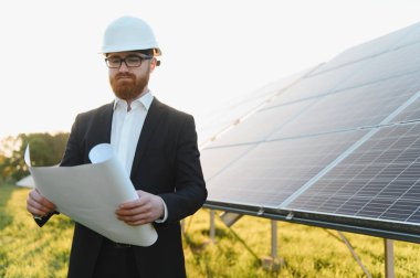 Sert başlıklı yatırımcı, yenilenebilir enerji ve sürdürülebilir kalkınma yatırımlarını sembolize ederek bir güneş paneli çiftliğinin planlarını gözden geçiriyor