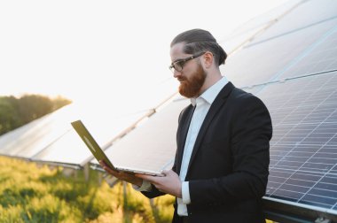 Günbatımında sürdürülebilir bir yenilenebilir enerji santralinde fotovoltaik güneş panellerini analiz eden bir iş adamı