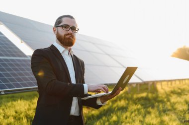 Günbatımında büyük bir güneş paneli çiftliğine yapılan güneş paneli yatırımlarını analiz eden bir iş adamı