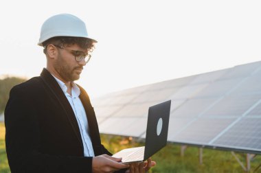 Arap işadamı güneş panellerini gün batımında incelerken dizüstü bilgisayar kullanarak yenilenebilir enerjiye yatırım yapıyor.
