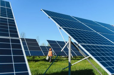 Açık mavi gökyüzü altında sürdürülebilir enerji ve çevre korumasını destekleyen büyük bir fotovoltaik tesisi denetleyen elektrik mühendisi