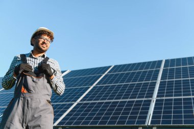 Güneş paneli kurulumu üzerinde çalışan sert bir şapka ve eldiven giyen teknisyen yenilenebilir enerji ve sürdürülebilir teknolojiyi vurguluyor