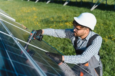 Yetenekli teknisyen, yeşil bir alanda yenilenebilir enerji çözümleri geliştirerek büyük ölçekli bir projede güneş enerjisi panelleri kurmak için bir tornavida kullanıyor.