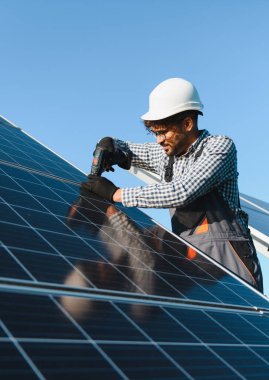 Güvenlik kaskı ve iş tulumuyla orta doğu mühendisi güneşli bir günde bir tornavida kullanarak güneş paneli kuruyor.