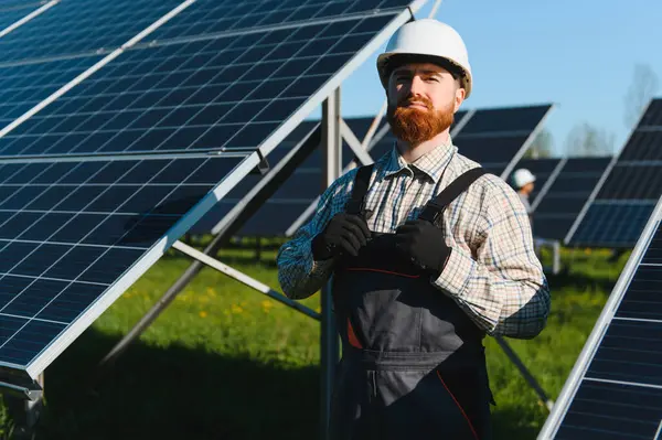 Kızıl kafalı mühendis, büyük bir güneş enerjisi santraline fotovoltaik paneller yerleştirirken iş kıyafetlerini ayarlıyor.