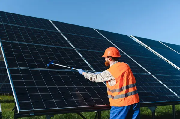 Erkek teknisyen fotovoltaik panelleri özel bir aletle temizliyor ve güneş çiftliğinden maksimum enerji üretimini sağlıyor.