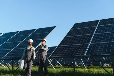 İki mühendis bir güneş enerjisi santralinde yürürken, aktif olarak güneş panelleri kurarken ve yenilenebilir enerji çözümleri geliştirirken iş birliği yapıyorlar.