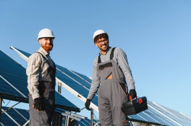 İki çok ırklı mühendis birlikte çalışarak büyük bir güneş enerjisi istasyonuna güneş panelleri kuruyor.
