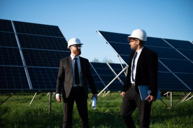 Güneş paneli çiftliğinde proje tartışması yapan iki mühendis, planları gözden geçirir ve bir dizüstü bilgisayardaki verileri analiz ederler.