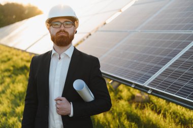 Günbatımında güneş paneli çiftliğini inceleyen planlı bir mühendis yenilenebilir enerji ve sürdürülebilir gelişimi somutlaştırıyor.