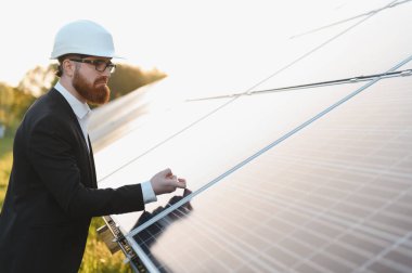 Takım elbiseli bir yatırımcı, güneş enerjisi potansiyelini ön plana çıkaran canlı bir günbatımında güneş panellerini denetliyor.