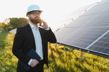 Yatırımcı güneş panellerini gün batımında incelerken akıllı telefon kullanıyor ve tablet tutuyor.