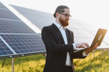 Yenilenebilir enerji yatırımları için güneş çiftliğindeki fotovoltaik güneş panellerini analiz eden bir iş adamı