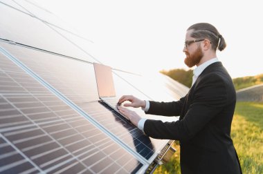 Bir güneş enerjisi santralindeki fotovoltaik panelleri analiz eden bir iş adamı gün batımının canlı renklerini yakalıyor.
